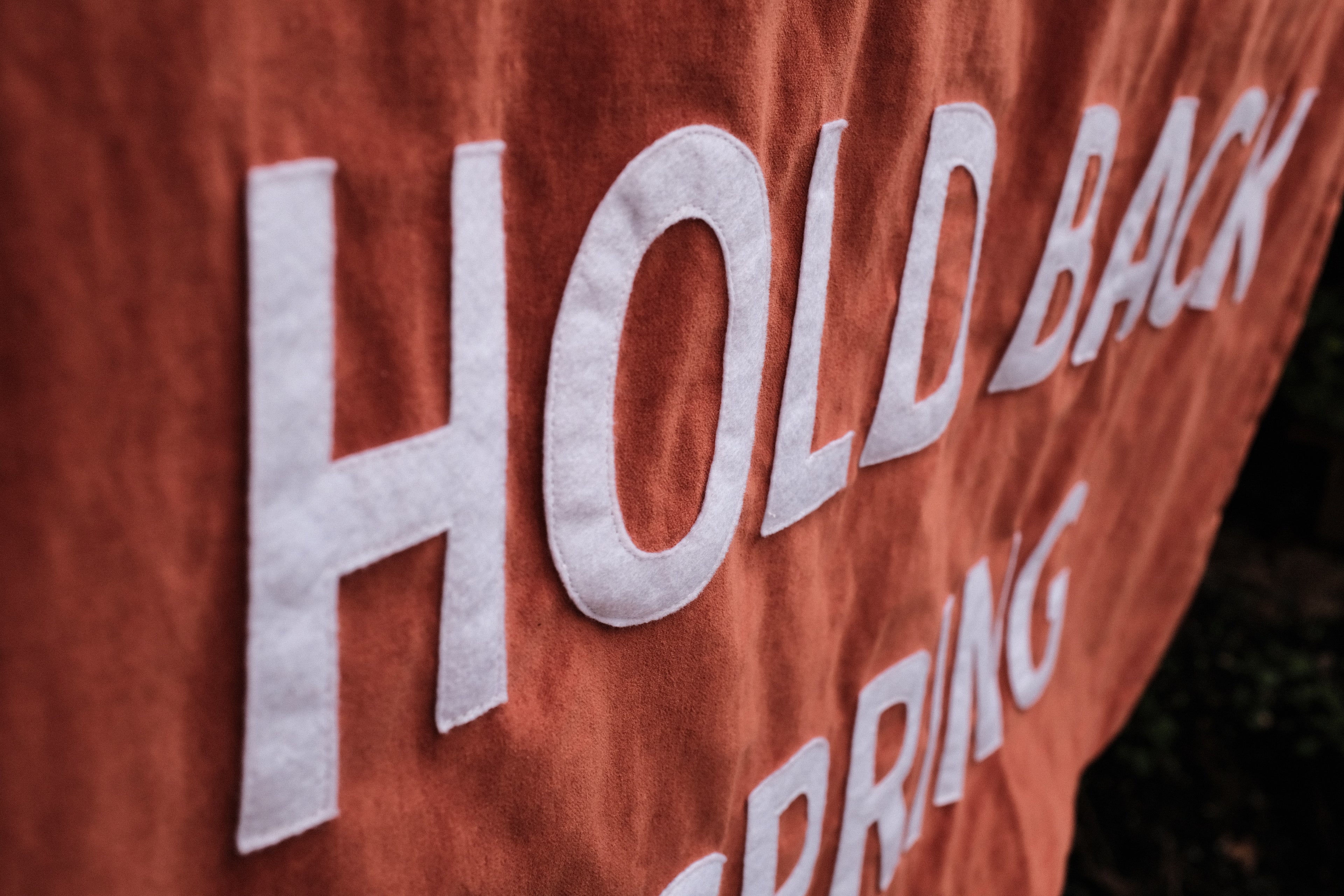 Text 'HOLD BACK SPRING' on an orange velvet banner