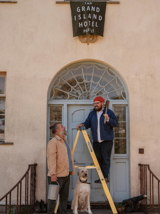 Banjo on a stepladder with Ro and Grampa outside the blue door to The Grand Island Hotel on Ulva with a green velvet banner above