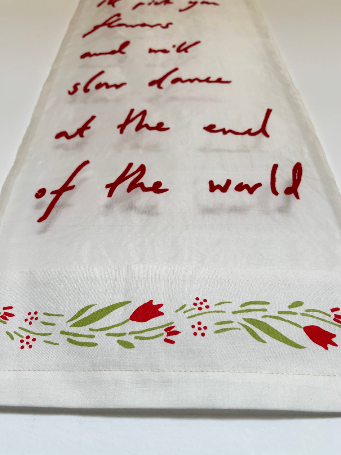 Textile artwork with red lettering which reads "I'll pick you flowers and we'll slow dance at the end of the world"
