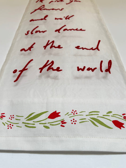 Textile artwork with red lettering which reads "I'll pick you flowers and we'll slow dance at the end of the world"