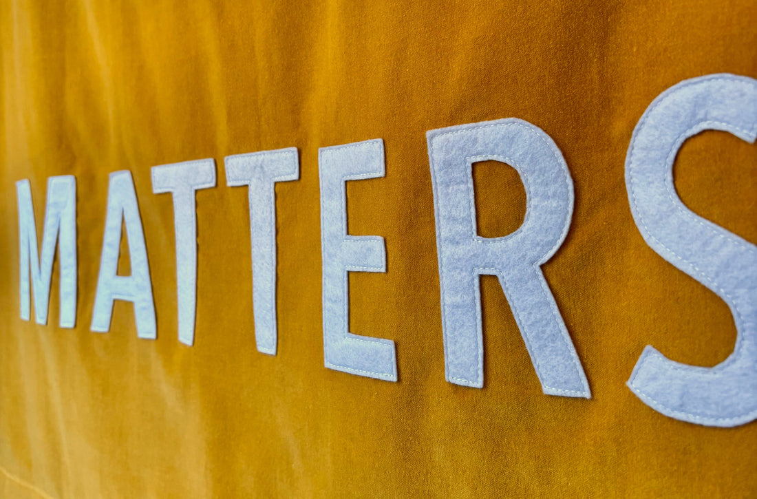 Close up of "Matters" stitched on a yellow velvet banner