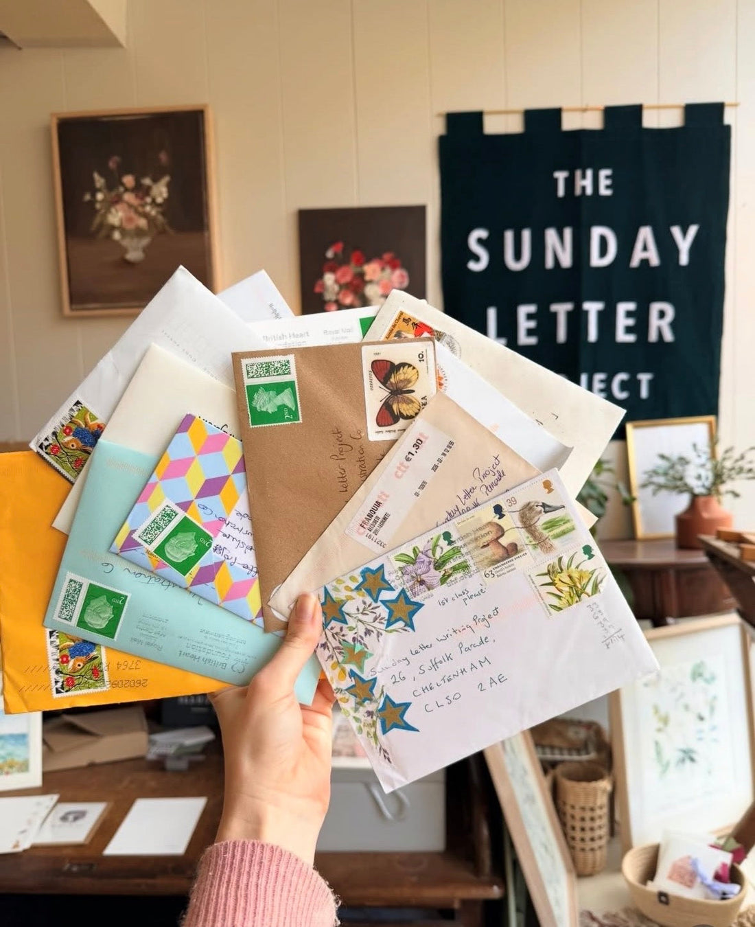 Handwritten letters held in front of a shop display with handmade banner and floral picture