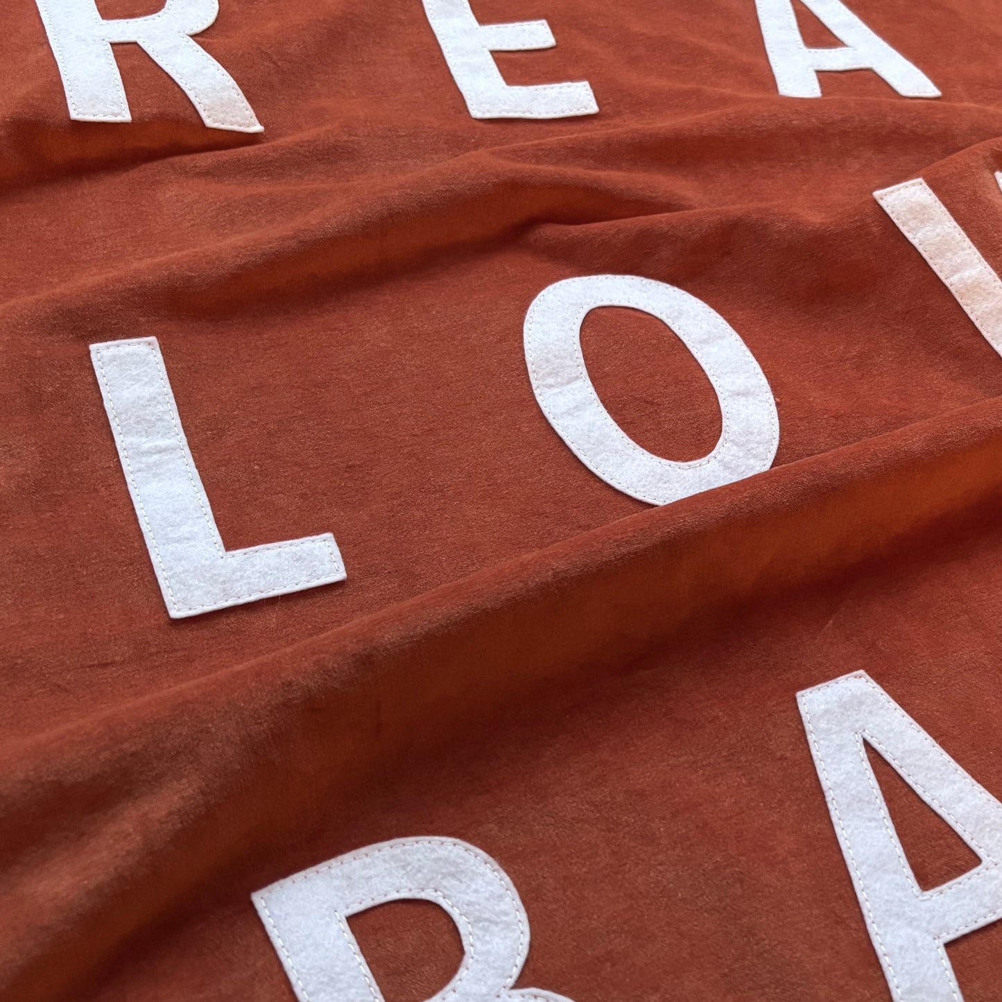 Close up of burnt orange velvet handmade banner with white felt letters.