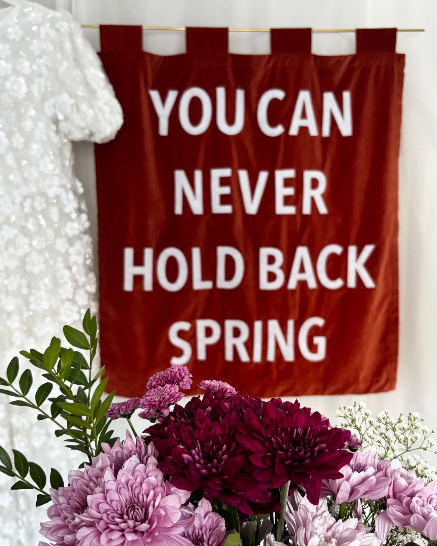 An orange velvet banner with "YOU CAN NEVER HOLD BACK SPRING" with a sequinned wedding dress and bouquet of pink flowers.