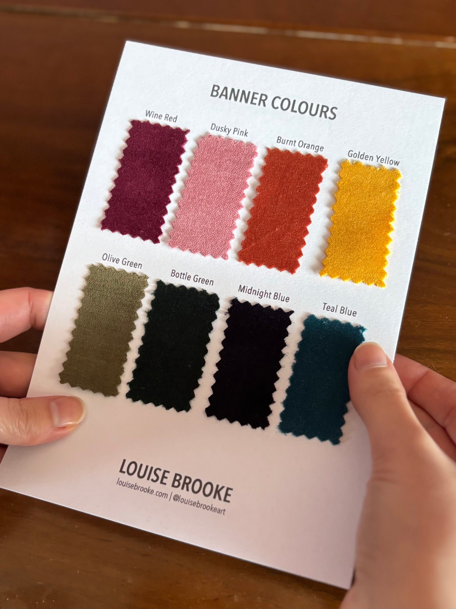 Color swatch card held by a person with color names and swatches on a wooden surface