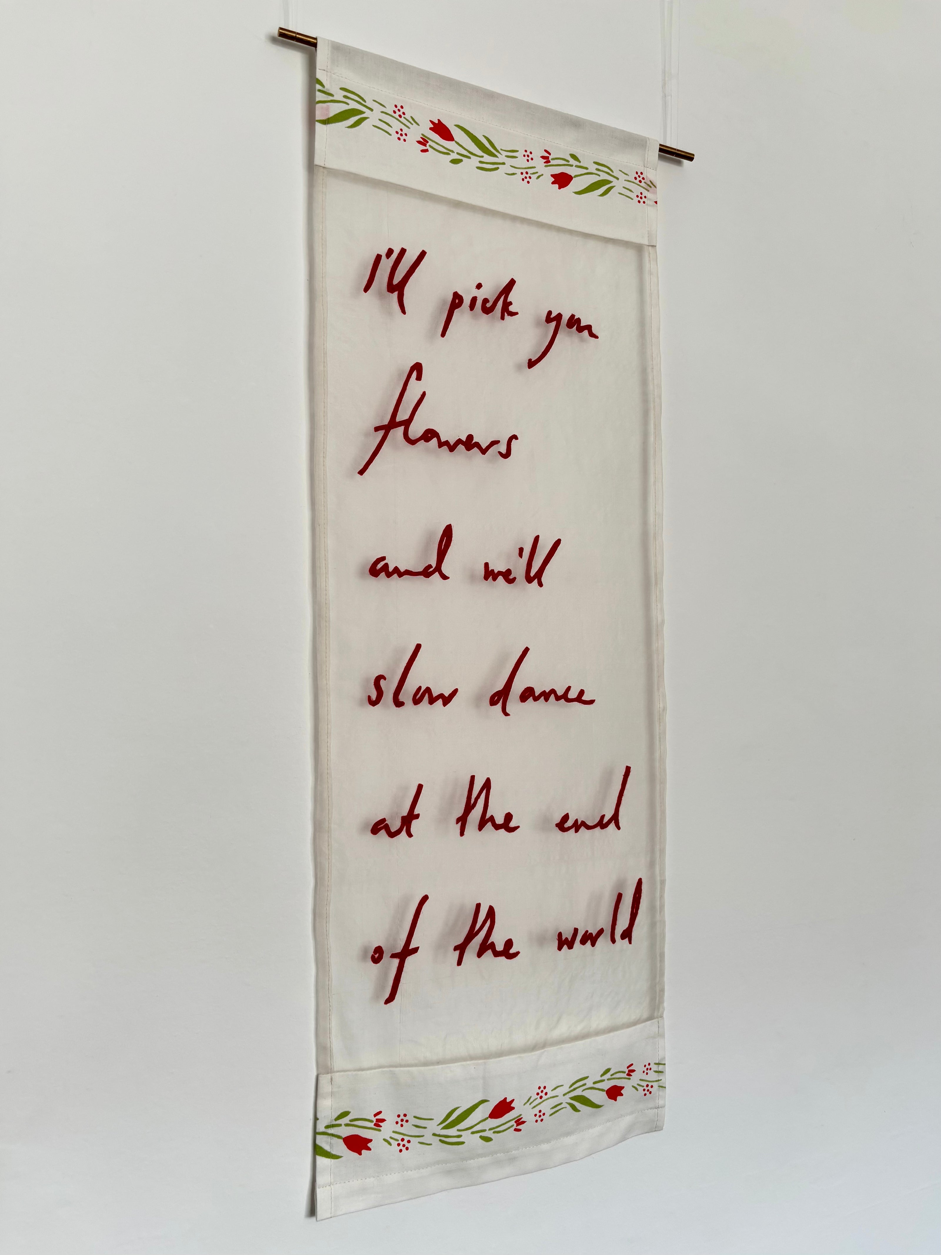 Textile with embroidered red text and floral patterns on a white background