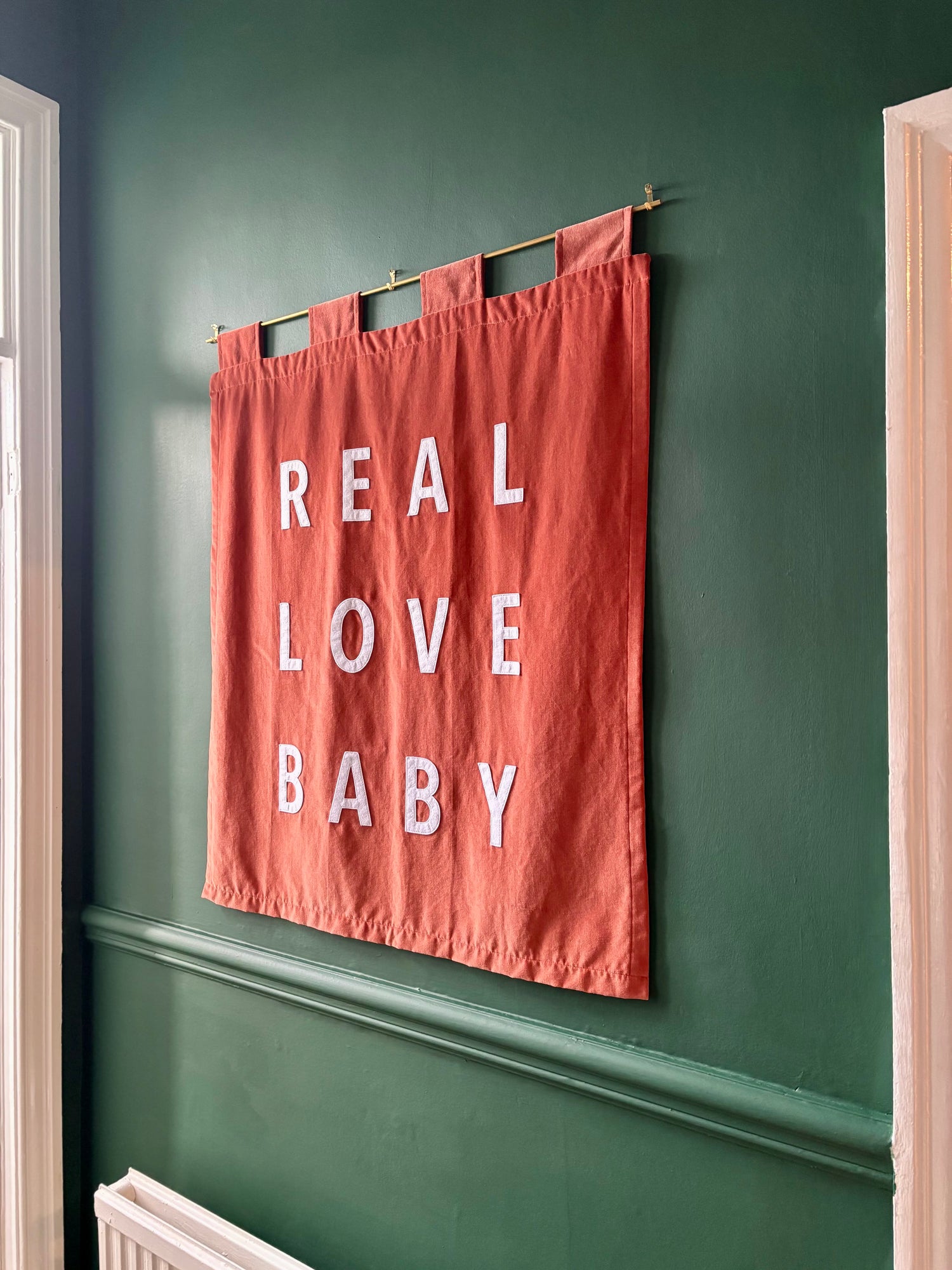 Orange velvet handmade banner with 'REAL LOVE BABY' on a green wall