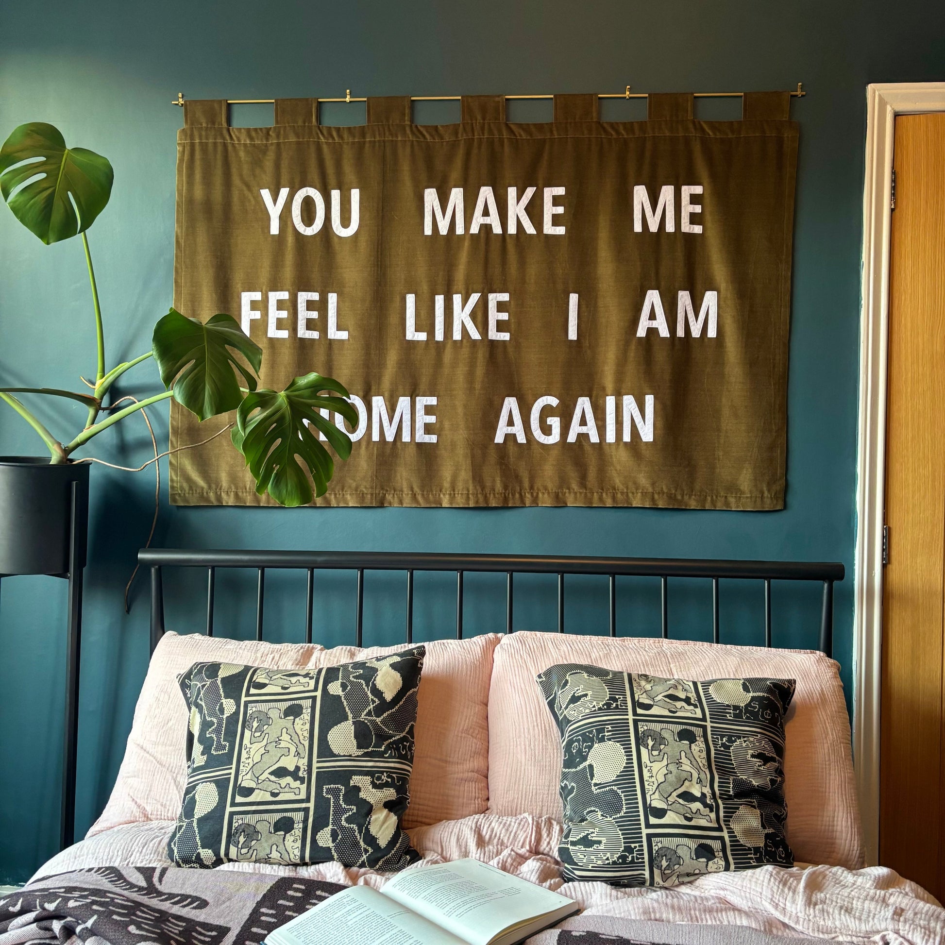 Green banner above a bed which reads "YOU MAKE ME FEEL LIKE I AM HOME AGAIN"