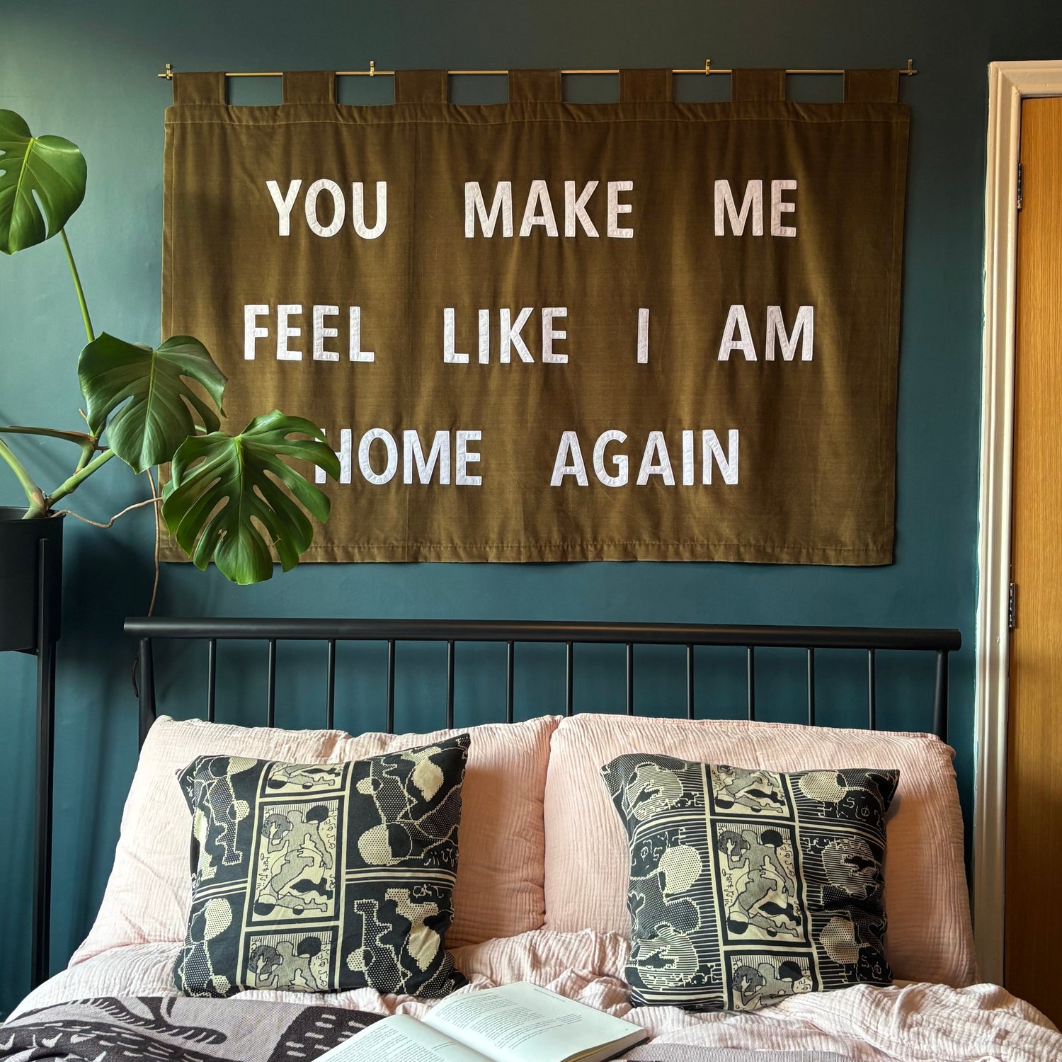 Handmade banner in olive green which reads "YOU MAKE ME FEEL LIKE I AM HOME AGAIN" above a bed