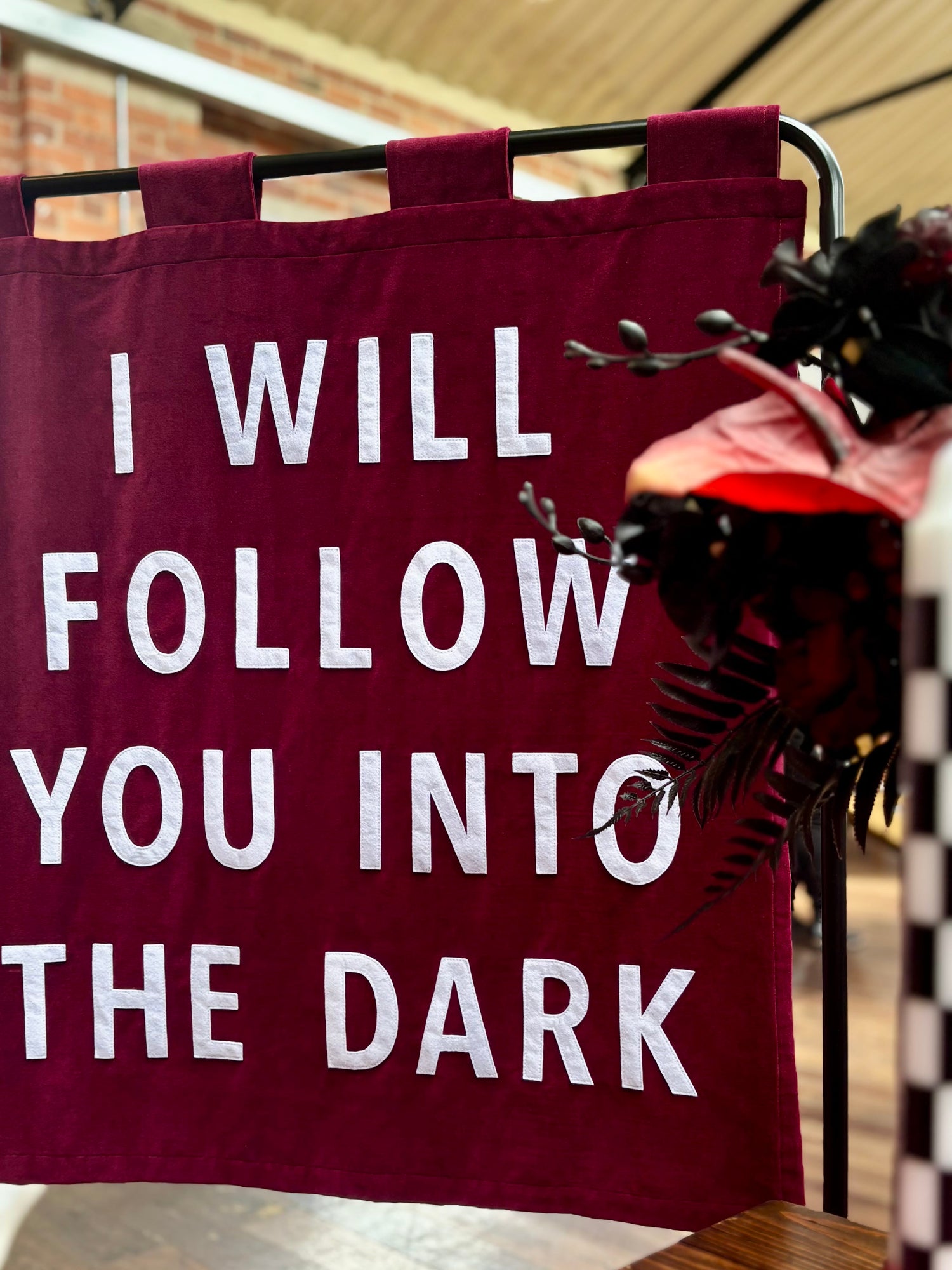 Red banner with white text 'I WILL FOLLOW YOU INTO THE DARK' in front of a blurred indoor background.