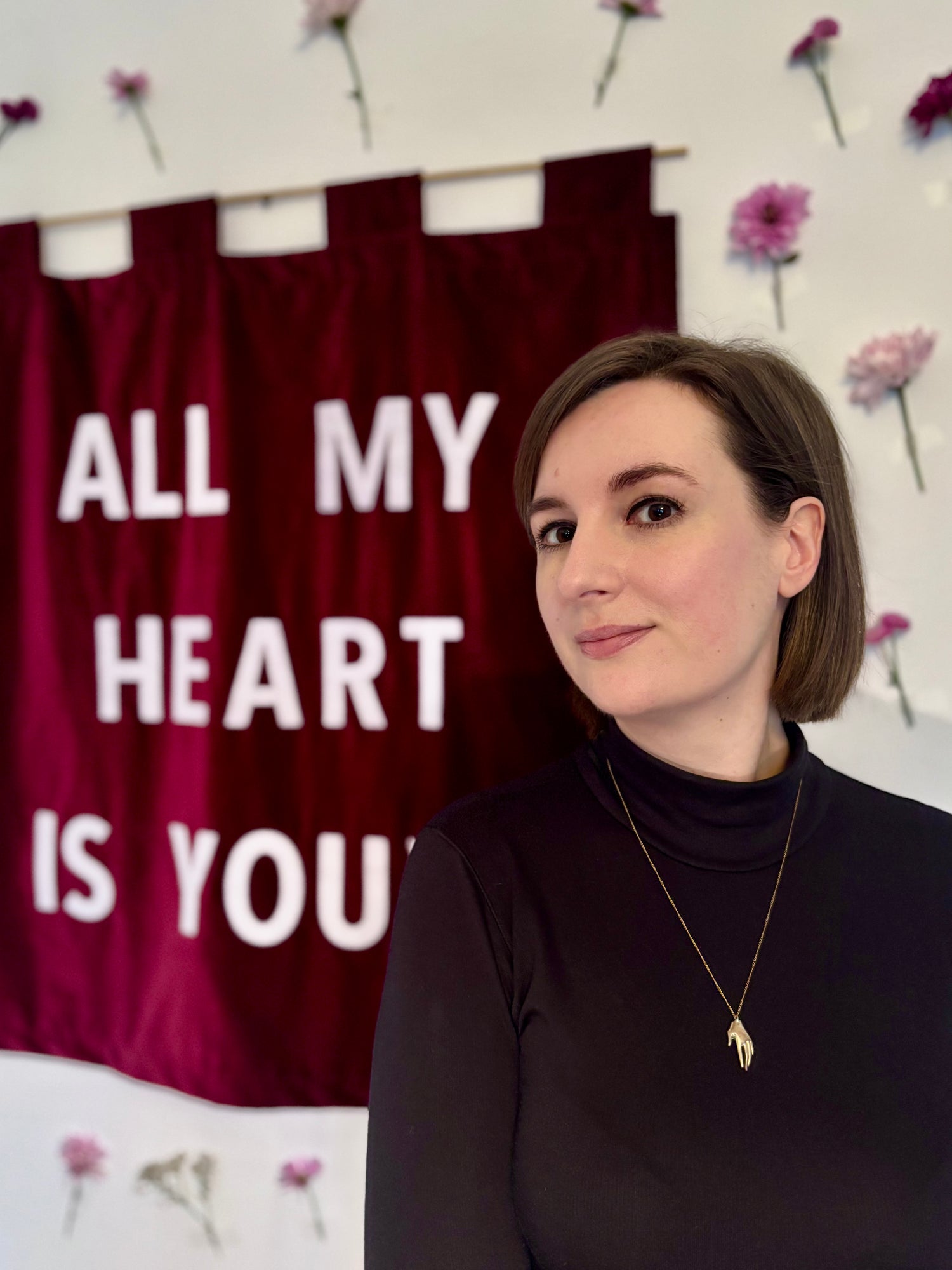 Louise Brooke standing in front of a red velvet banner with 'All My Heart Is Yours' text and floral decorations.