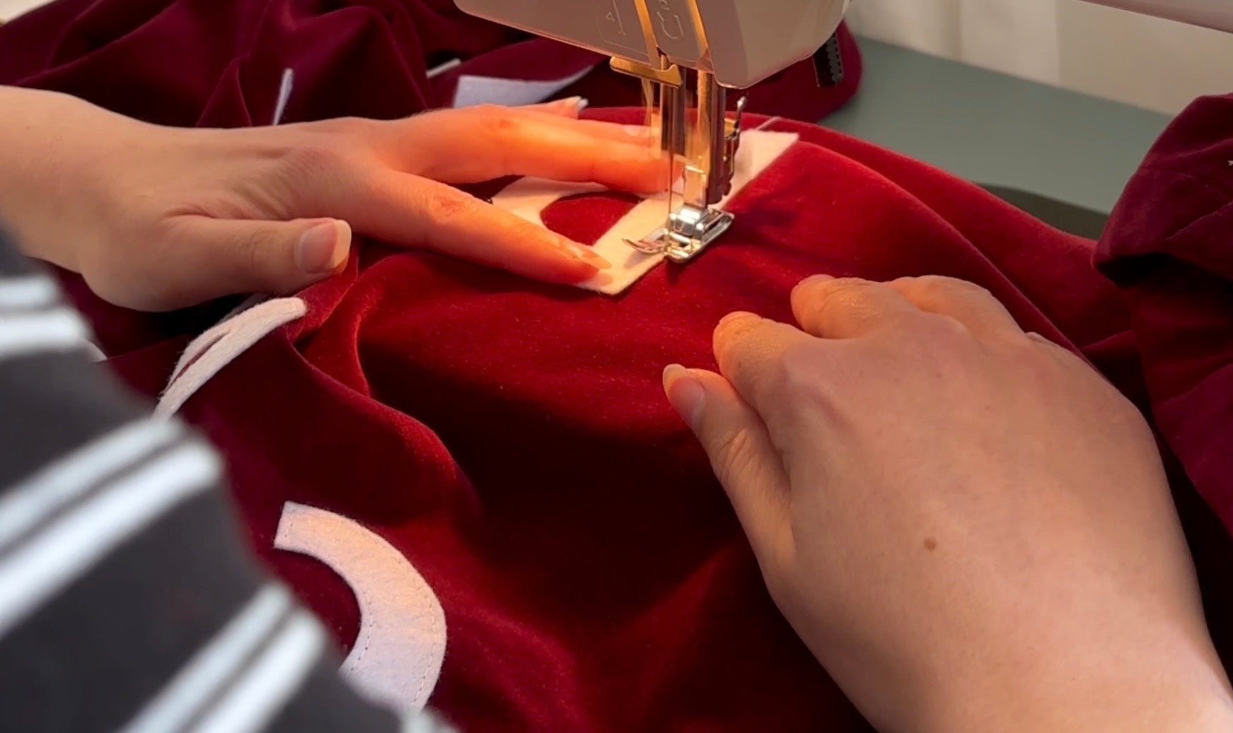 Person sewing a red handmade velvet banner with white lettering using a sewing machine.