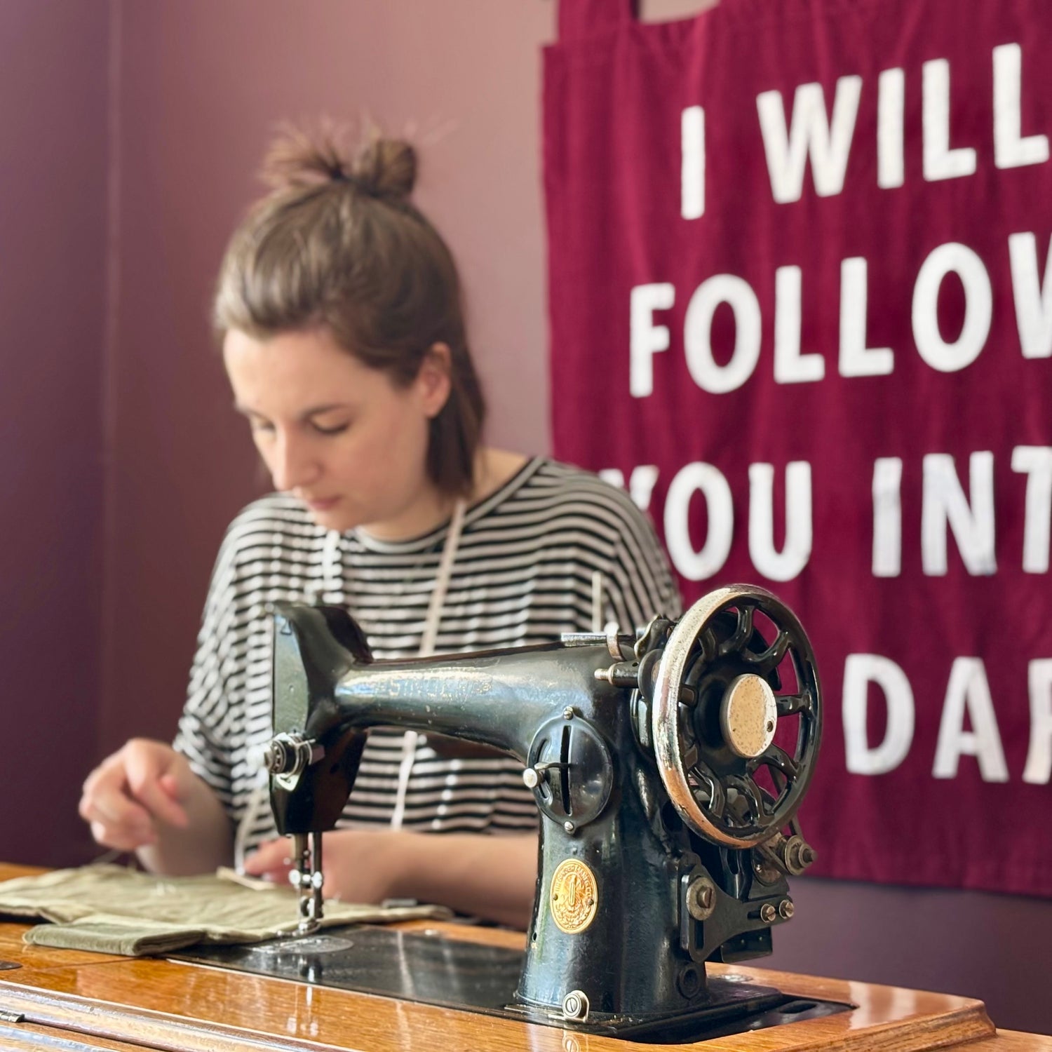 Person working on an old-fashioned sewing machine with a handmade banner in the background.