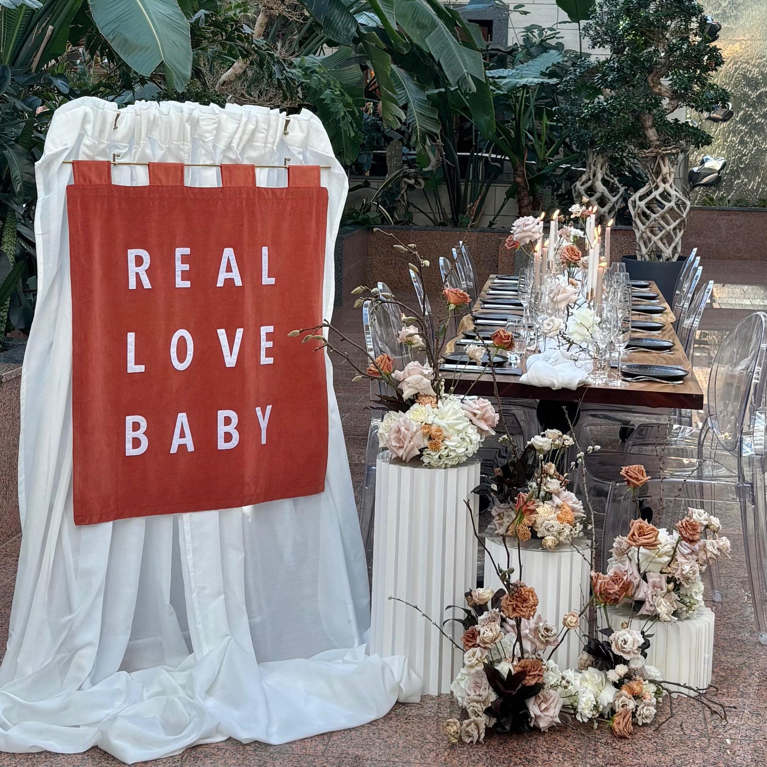 Orange wedding banner which reads "REAL LOVE BABY" next to a wedding table and flowers