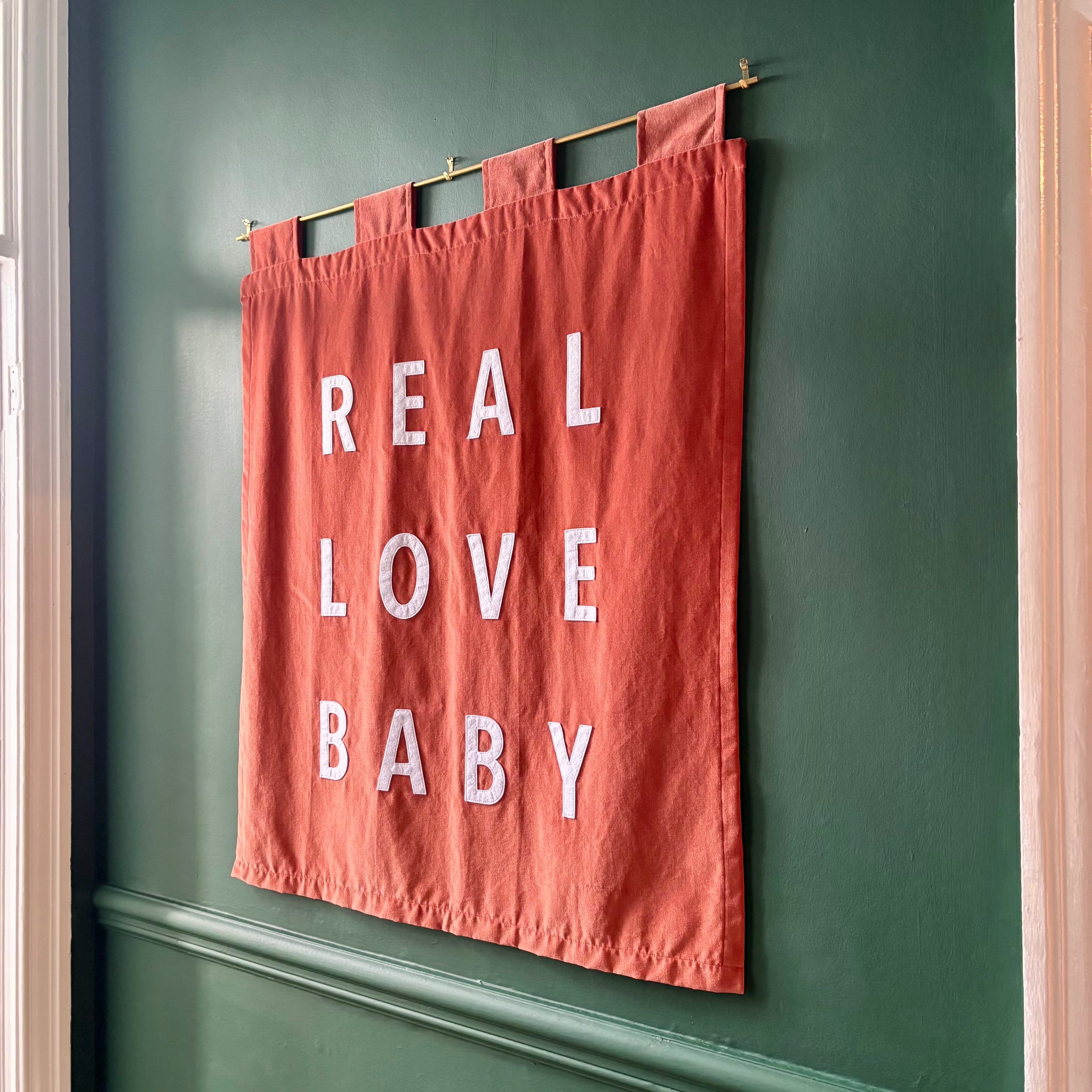 Orange velvet handmade banner with 'REAL LOVE BABY' text hanging on a green wall