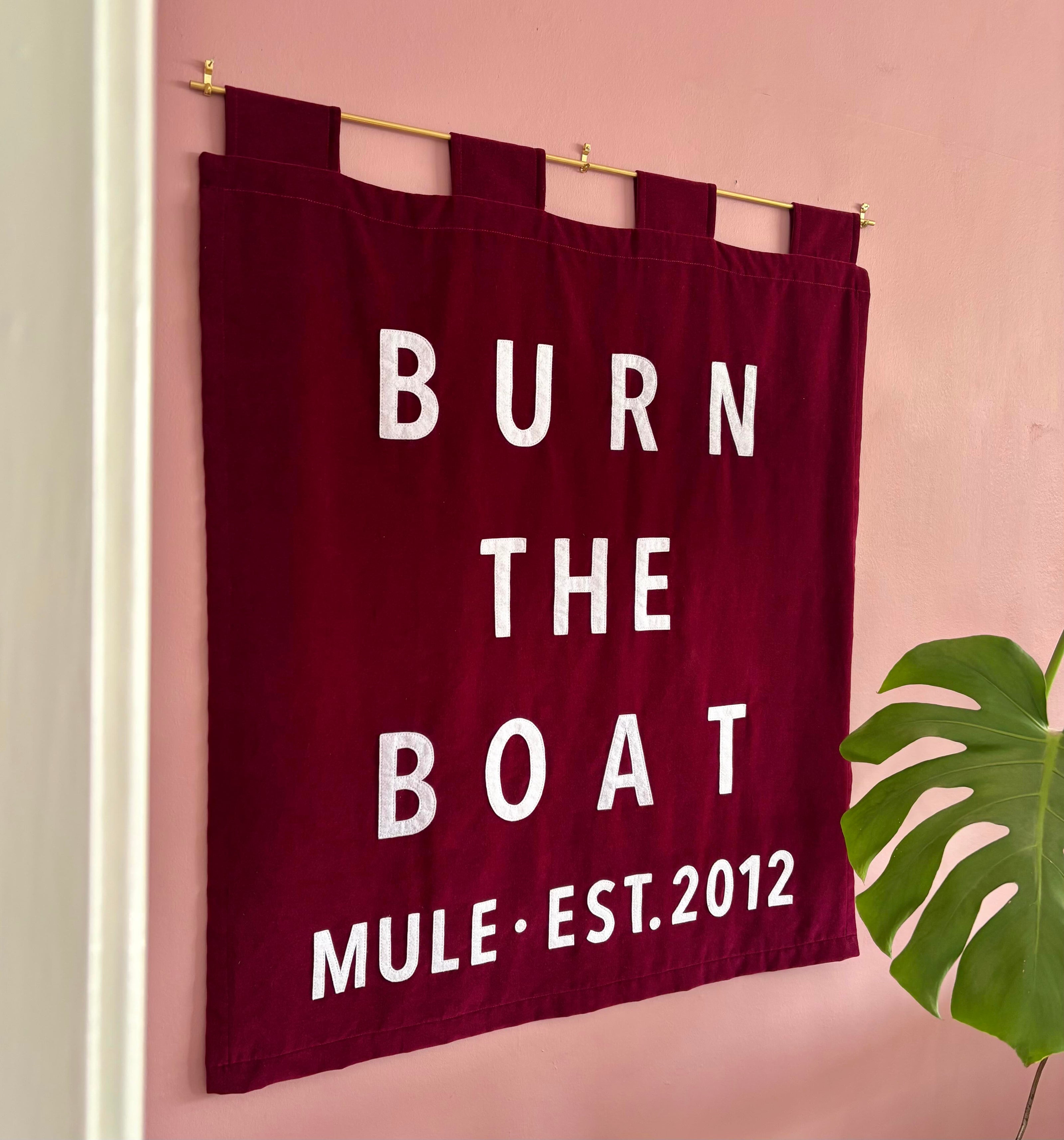 Red banner with white text 'Burn The Boat' and 'Mule Est. 2012' hanging on a pink wall.