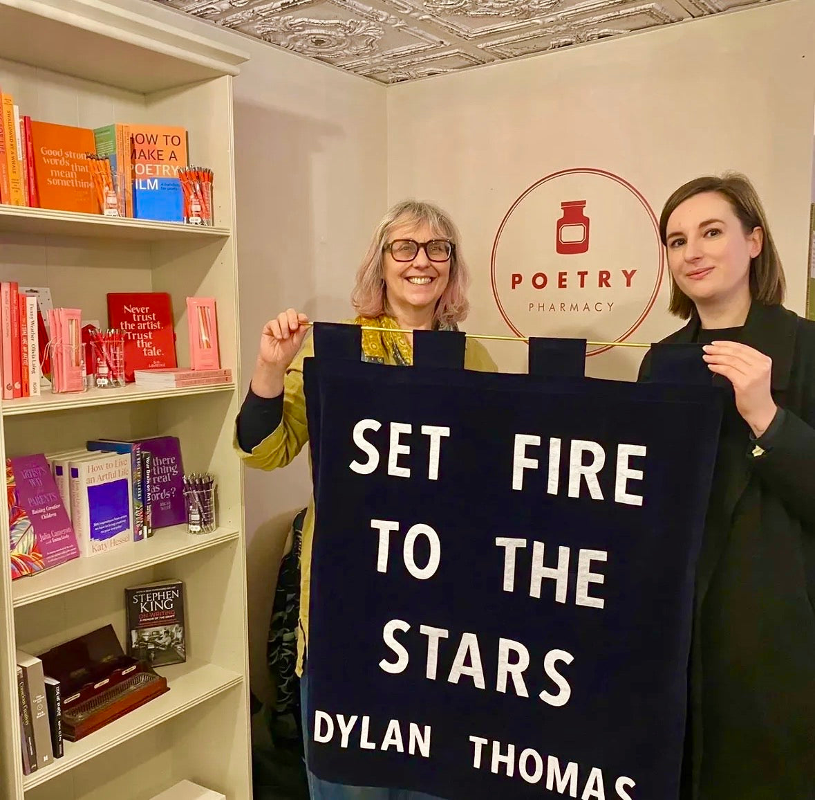 Two people holding a banner with text in the Poetry Pharmacy bookshop