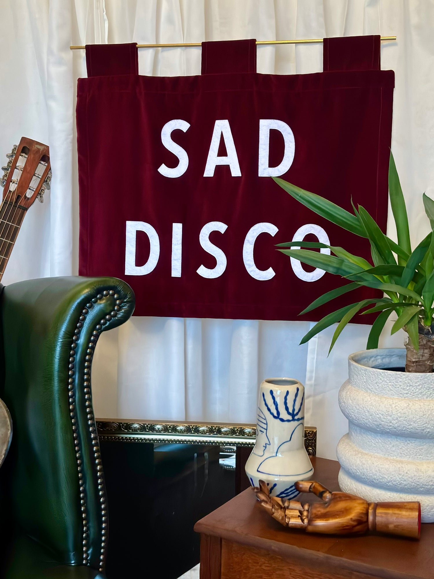 Red banner with 'SAD DISCO' text hanging in a room with a green chair, plant, and decorative items.