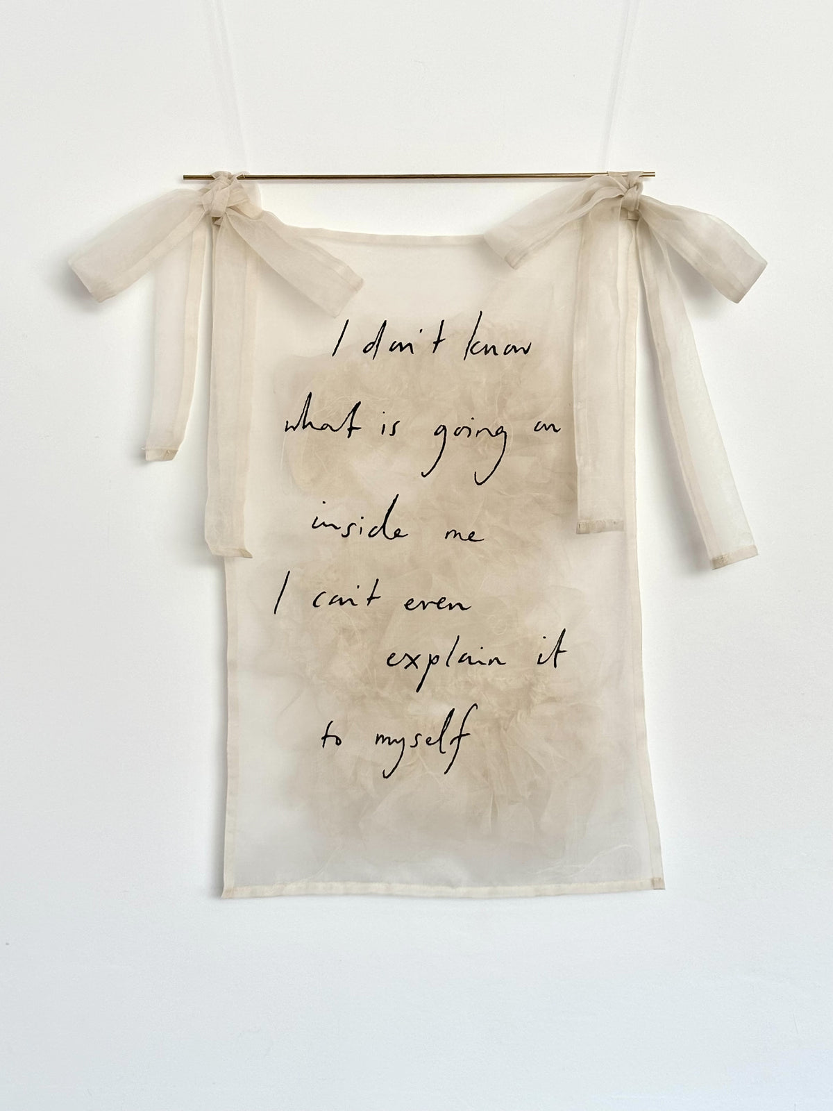 A sheer silk wall hanging with tied side bows and a brass pole, featuring handwritten black text that reads, 'I don't know what is going on inside me I can't even explain it to myself,' displayed against a white wall.