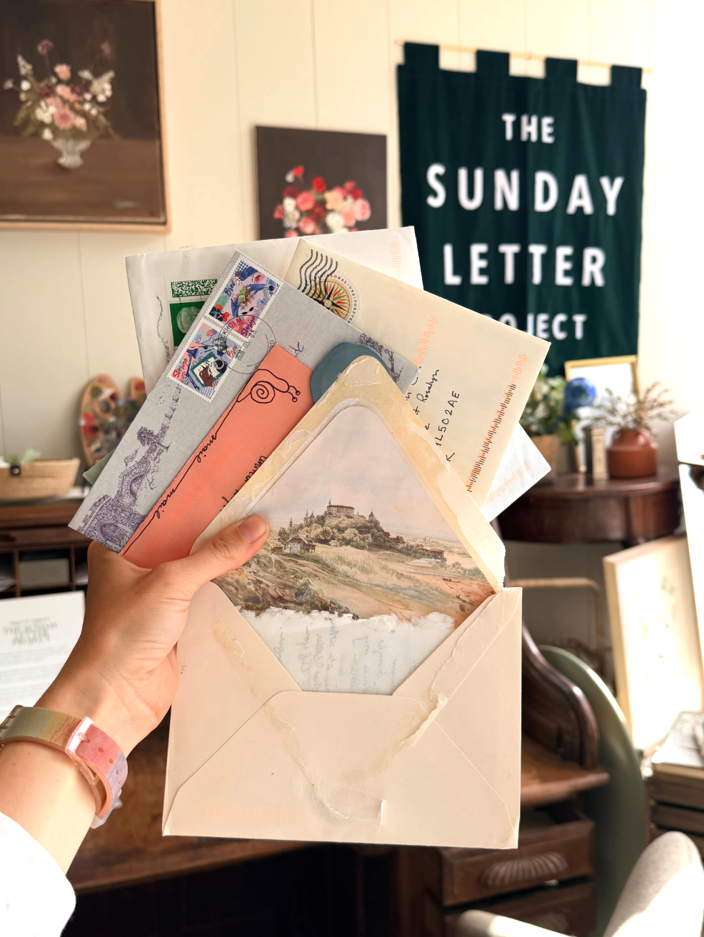 Hand holds letters in front of shop with vintage furniture, floral paintings and a handmade velvet banner which reads "THE SUNDAY LETTER PROJECT"