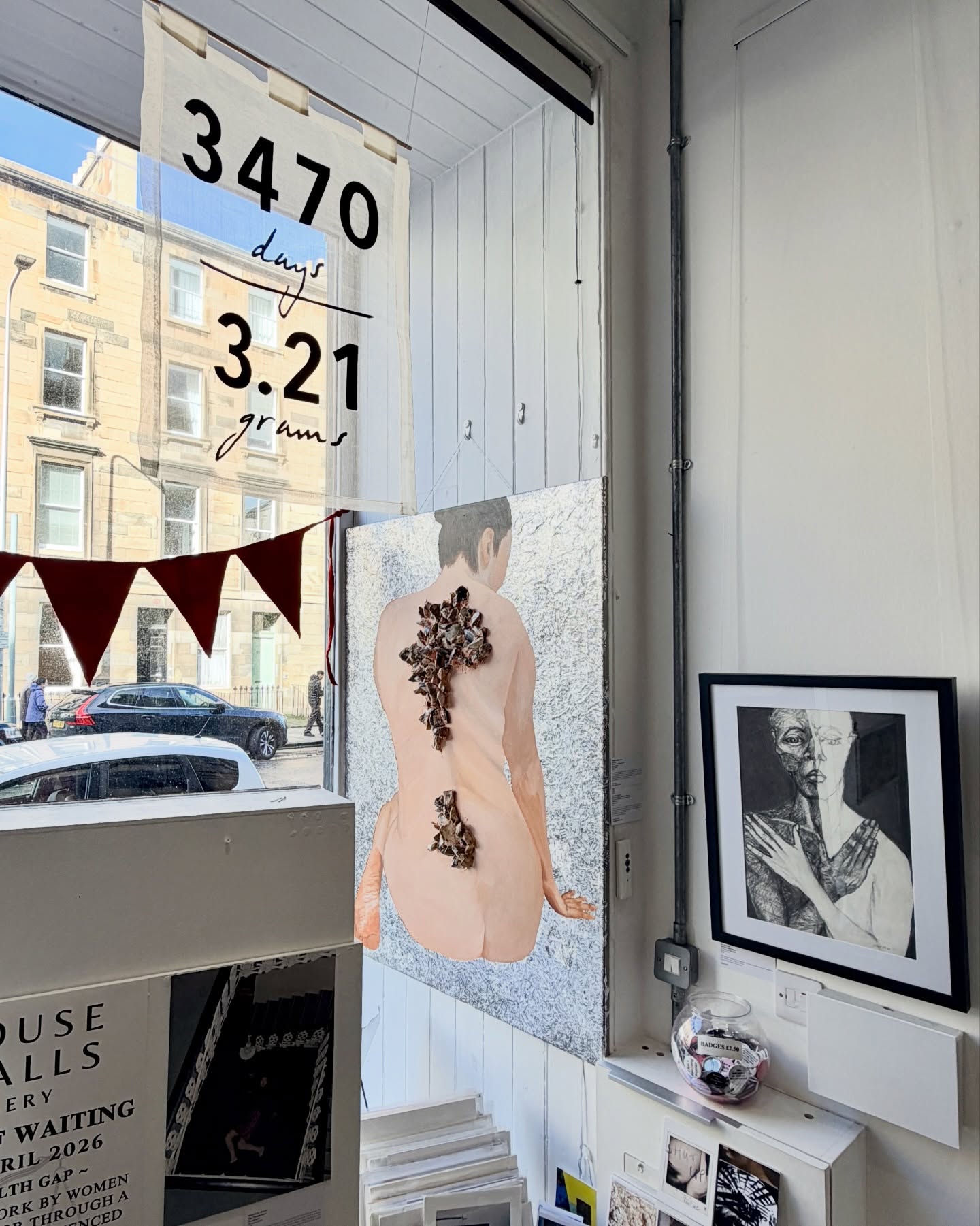 Art gallery window with a artwork of a nude figure and banner.