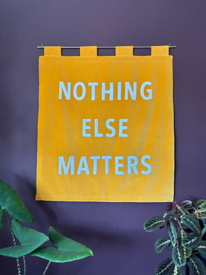 Yellow velvet banner with 'NOTHING ELSE MATTERS' text on a purple wall with plants.