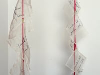 Video of A Void Dance, a kinetic textile sculpture which slowly spins. The sculpture is made of a thin brass arc which holds handwritten silk letters, suspended from red ribbon and suspender clasps.